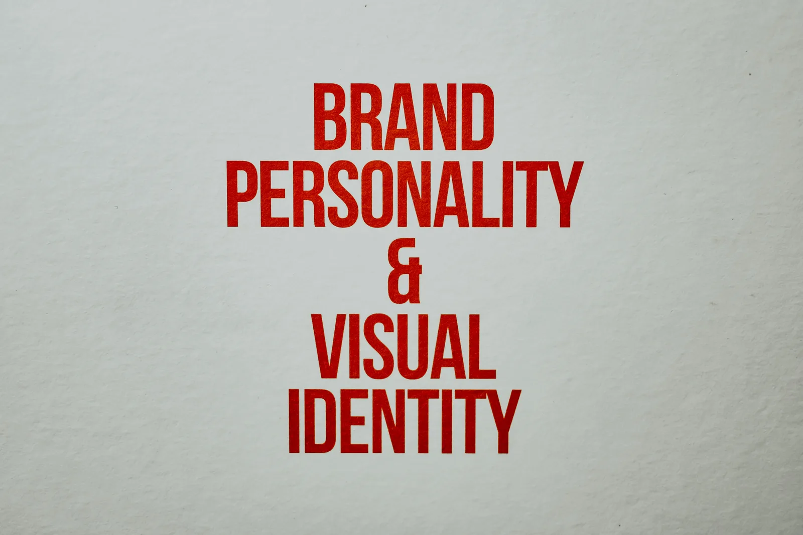 Kâğıt dokulu açık gri zeminde kırmızı büyük harflerle "Brand Personality & Visual Identity" yazısı